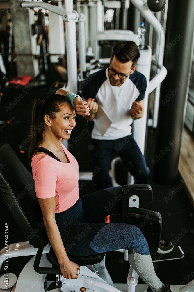 Young fit and attractive woman working out in modern gym together with her personal fitness instructor or coach. Young fit and attractive woman working out in modern gym together with her personal fitness instructor or coach.