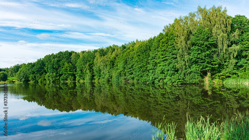 Symmetrical landscape with a beautiful forest lake, in the water of which deciduous forest is reflected. Mirror landscape. The forest is reflected in the water of the Dubrova lake. Nature harmony. Symmetrical landscape with a beautiful forest lake, in the water of which deciduous forest is reflected. Mirror landscape. The forest is reflected in the water of the Dubrova lake. Nature harmony.