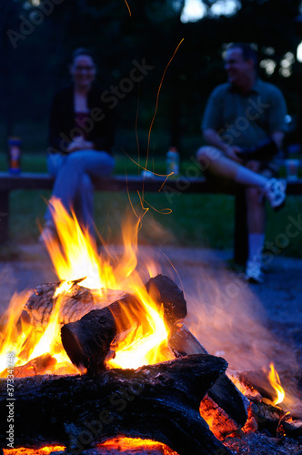 Man and a woman sitting by a campfire at dusk talking and laughing