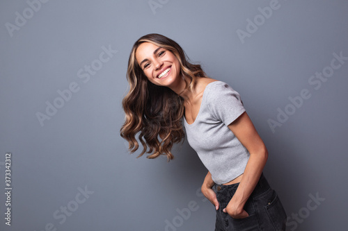 Laughing young woman standing against a gray wall.