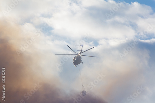 Fire-fighting helicopter against the background of smoke and sky
