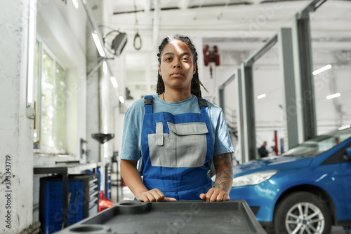 Exploring repairing. African american woman, professional female mechanic pulling, carrying tool box cart in auto repair shop. Car service, maintenance and people concept