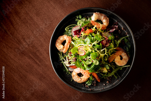 Shrimps salad with cherry tomatoes  cucumeber  avocado  lettuce and pomegranate on dish. Healthy seafood concept. Tasty grilled prawn shrimp and mix vegetable salad on black wood