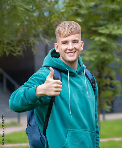 Handsome university cheerful student with backpack showing thumb up, like, approval gesture outdoors at campus. Young happy positive successful man look at camera and smiling, laughing. Get in college © Евгений Шемякин