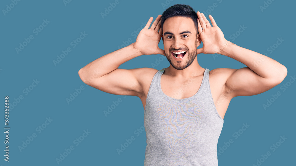 Young handsome man wearing swimwear and sleeveless t-shirt smiling cheerful playing peek a boo with hands showing face. surprised and exited Young handsome man wearing swimwear and sleeveless t-shirt smiling cheerful playing peek a boo with hands showing face. surprised and exited