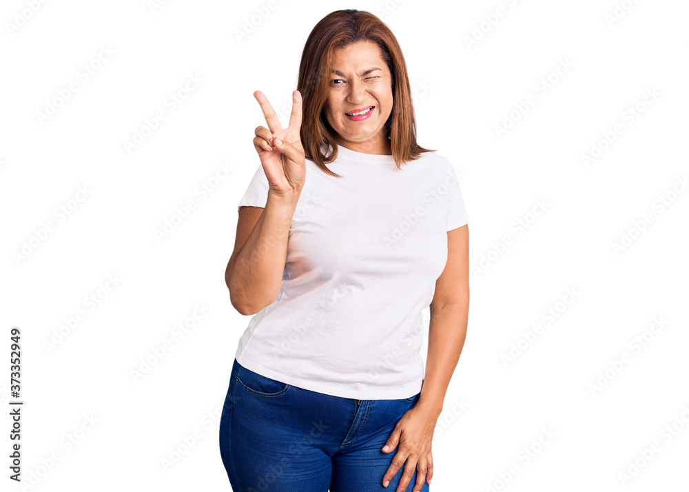 Middle age latin woman wearing casual white tshirt smiling with happy face winking at the camera doing victory sign with fingers. number two. Middle age latin woman wearing casual white tshirt smiling with happy face winking at the camera doing victory sign with fingers. number two.
