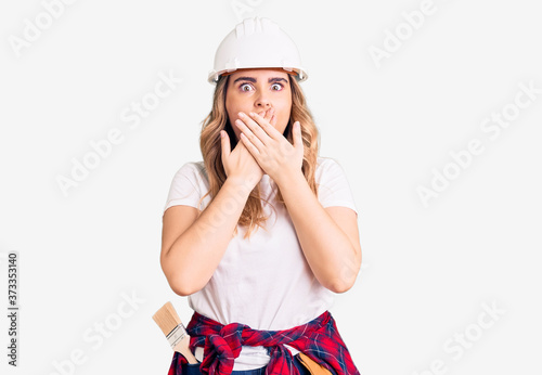 Young caucasian woman wearing security helmet shocked covering mouth with hands for mistake. secret concept. photo