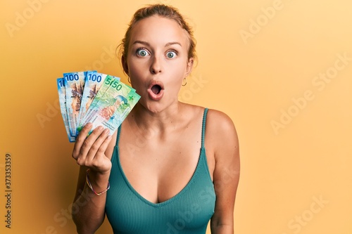 Beautiful caucasian woman holding swiss franc banknotes scared and amazed with open mouth for surprise, disbelief face