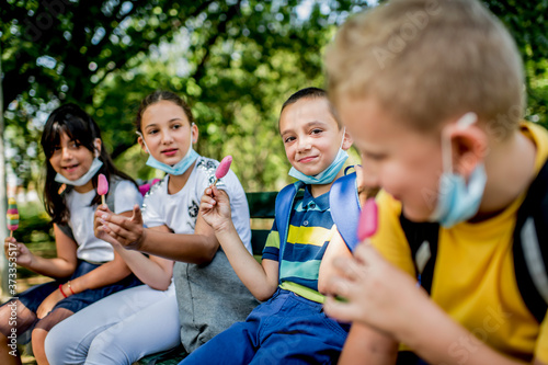 Group of children eating ice cream outside. They are wearing a protective face mask down.