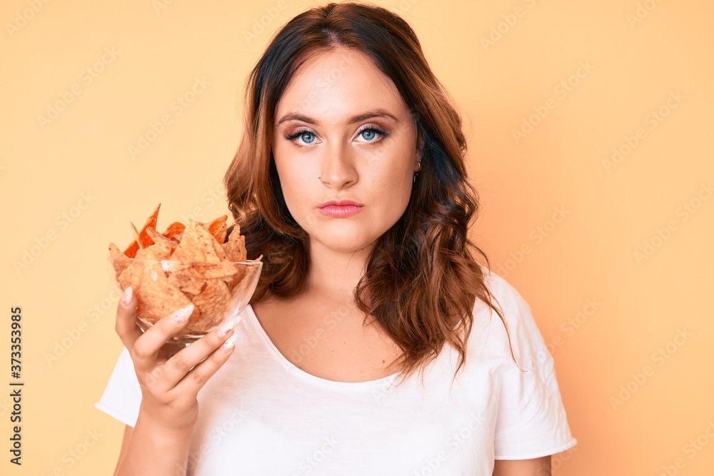 Young beautiful caucasian woman holding nachos potato chips thinking attitude and sober expression looking self confident