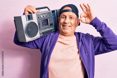 Senior handsome grey-haired modern man listening to music using vintage boombox doing ok sign with fingers, smiling friendly gesturing excellent symbol