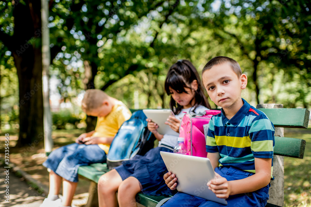 Back to school during quarantine. Children with backpacks wearing protective face mask and using mobile phones and digital tablets. Back to school during quarantine. Children with backpacks wearing protective face mask and using mobile phones and digital tablets.