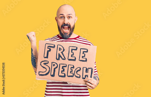 Young handsome man holding free speech banner screaming proud, celebrating victory and success very excited with raised arms