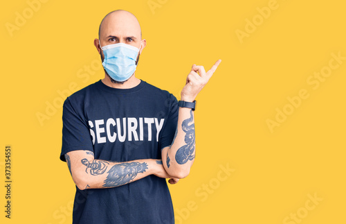 Young handsome man wearing security t shirt and medical mask smiling happy pointing with hand and finger to the side