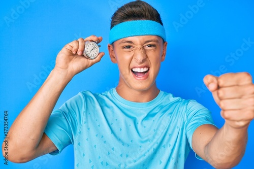 Young hispanic boy holding stopwatch annoyed and frustrated shouting with anger, yelling crazy with anger and hand raised