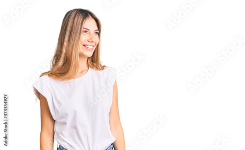 Beautiful caucasian woman with blonde hair wearing casual white tshirt looking away to side with smile on face, natural expression. laughing confident.