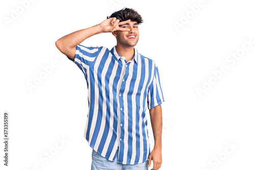 Young hispanic man wearing casual clothes doing peace symbol with fingers over face, smiling cheerful showing victory