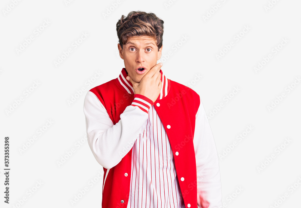 Young handsome man wearing baseball uniform looking fascinated with disbelief, surprise and amazed expression with hands on chin Young handsome man wearing baseball uniform looking fascinated with disbelief, surprise and amazed expression with hands on chin