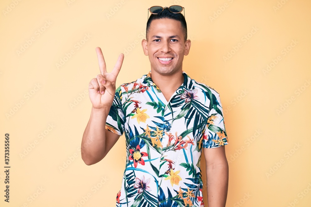 Young handsome latin man wearing summer clothes showing and pointing up with fingers number two while smiling confident and happy. Young handsome latin man wearing summer clothes showing and pointing up with fingers number two while smiling confident and happy.