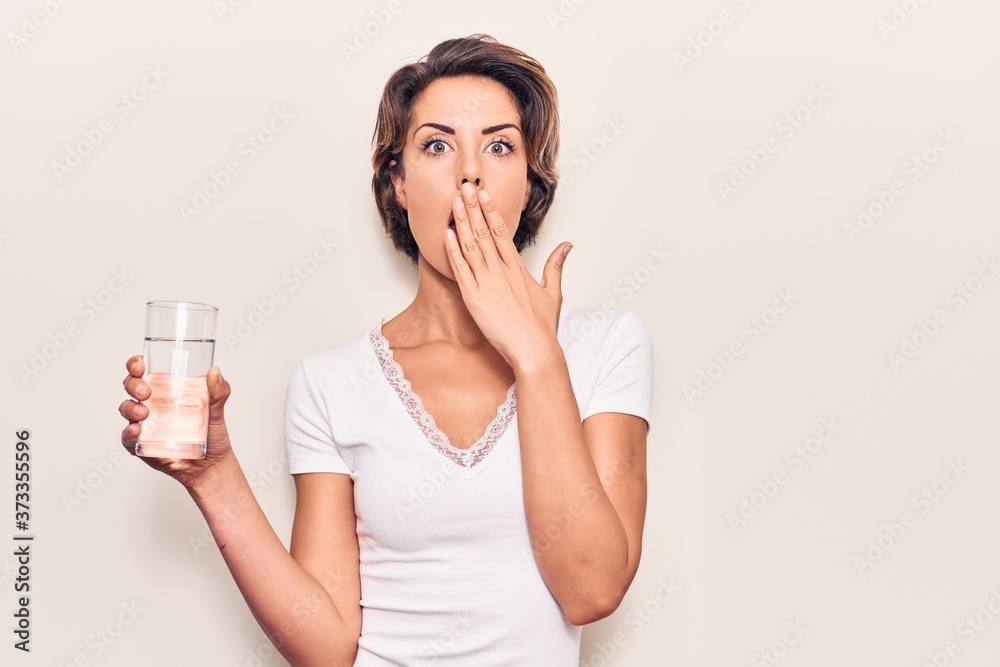 Young beautiful woman drinking glass of water covering mouth with hand, shocked and afraid for mistake. surprised expression Young beautiful woman drinking glass of water covering mouth with hand, shocked and afraid for mistake. surprised expression
