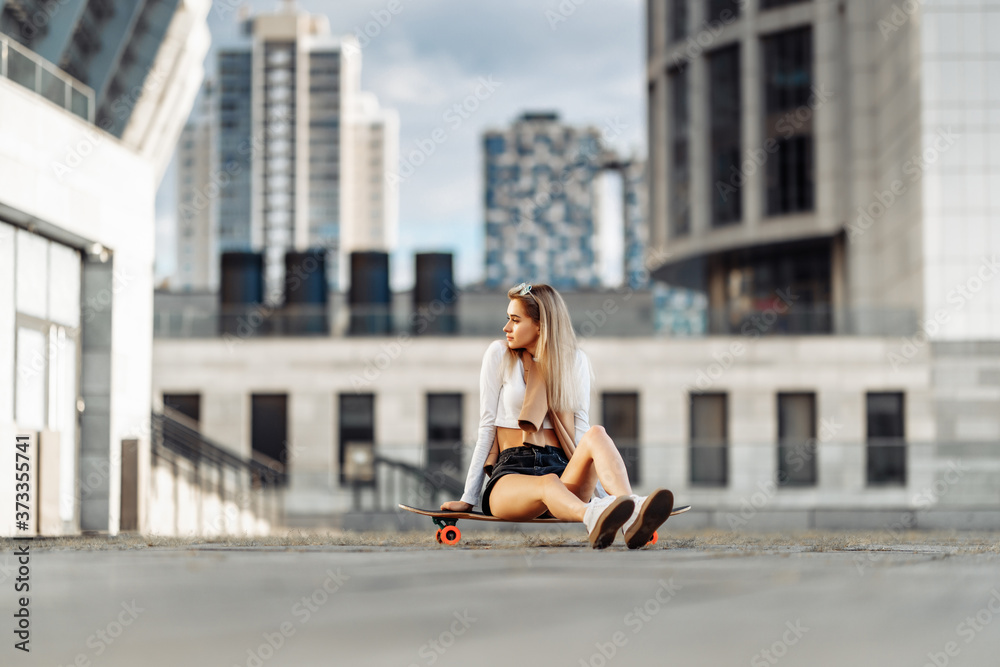 Fototapeta premium Beautiful woman sitting on a longboard. Evening big city.