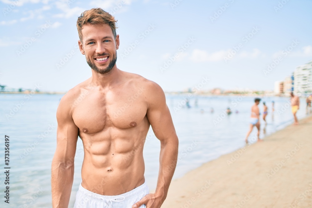Handsome fitness caucasian man at the beach on a sunny day showing muscular fitness body Handsome fitness caucasian man at the beach on a sunny day showing muscular fitness body
