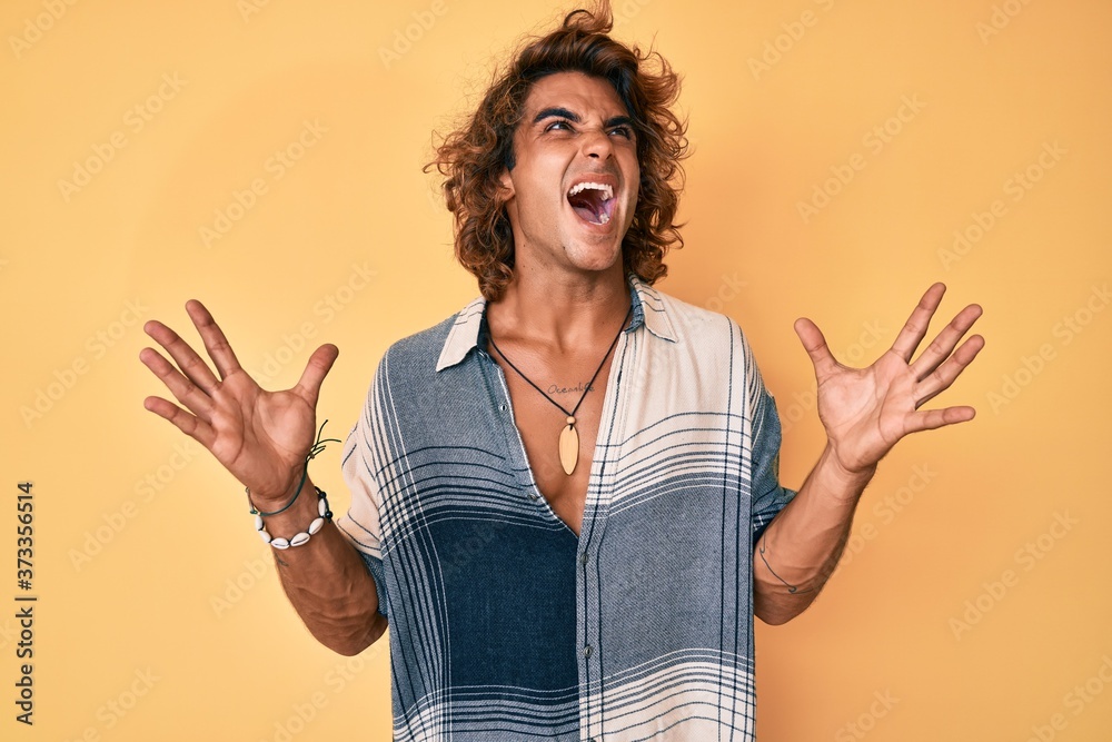 Young hispanic man wearing summer style crazy and mad shouting and yelling with aggressive expression and arms raised. frustration concept. Young hispanic man wearing summer style crazy and mad shouting and yelling with aggressive expression and arms raised. frustration concept.