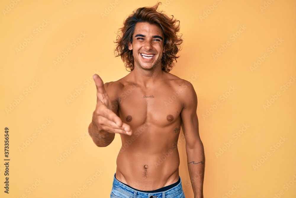 Young hispanic man standing shirtless smiling friendly offering handshake as greeting and welcoming. successful business.