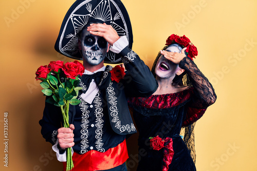 Young couple wearing mexican day of the dead costume holding roses stressed and frustrated with hand on head, surprised and angry face