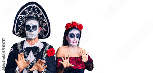 Young couple wearing mexican day of the dead costume over background disgusted expression, displeased and fearful doing disgust face because aversion reaction.