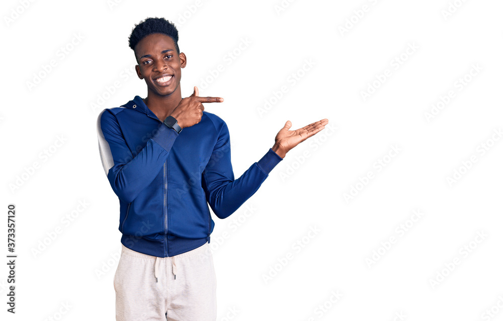 Young african american man wearing sportswear amazed and smiling to the camera while presenting with hand and pointing with finger. Young african american man wearing sportswear amazed and smiling to the camera while presenting with hand and pointing with finger.