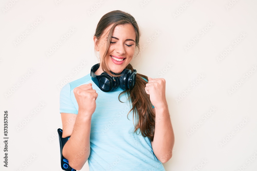 Beautiful young caucasian woman wearing gym clothes and using headphones excited for success with arms raised and eyes closed celebrating victory smiling. winner concept. Beautiful young caucasian woman wearing gym clothes and using headphones excited for success with arms raised and eyes closed celebrating victory smiling. winner concept.