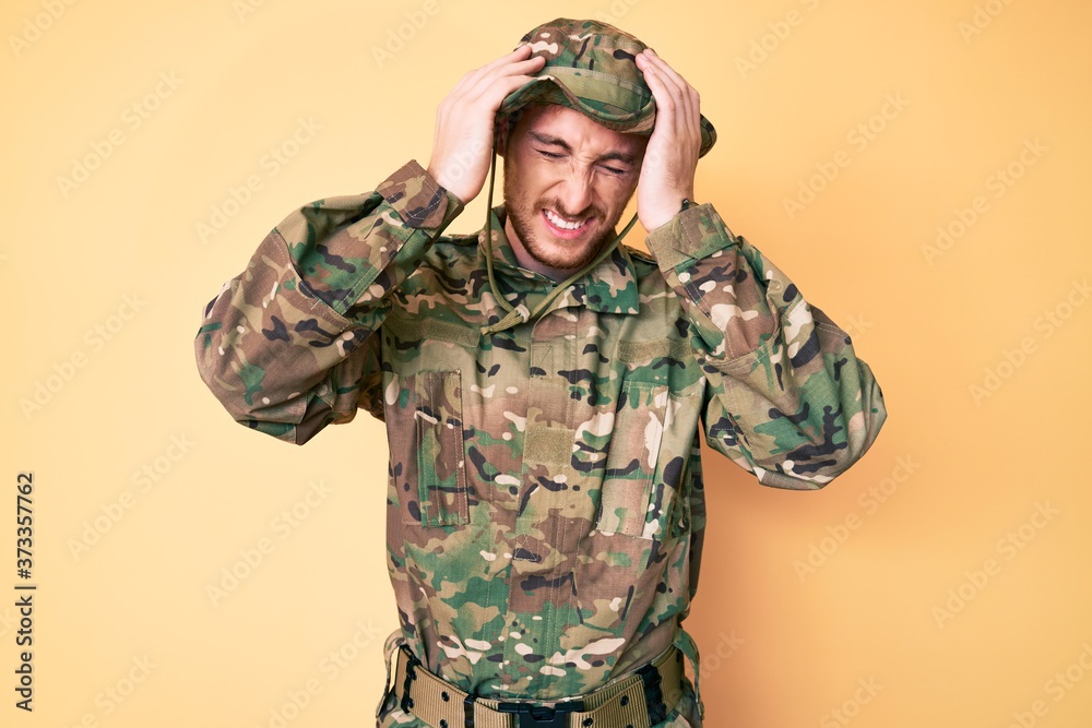 Young caucasian man wearing camouflage army uniform suffering from headache desperate and stressed because pain and migraine. hands on head.