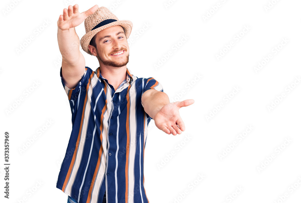 Young handsome caucasian man wearing summer hat looking at the camera smiling with open arms for hug. cheerful expression embracing happiness. Young handsome caucasian man wearing summer hat looking at the camera smiling with open arms for hug. cheerful expression embracing happiness.