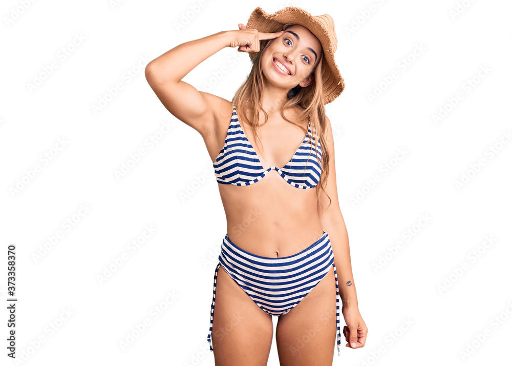 Young beautiful blonde woman wearing bikini and hat smiling pointing to head with one finger, great idea or thought, good memory Young beautiful blonde woman wearing bikini and hat smiling pointing to head with one finger, great idea or thought, good memory