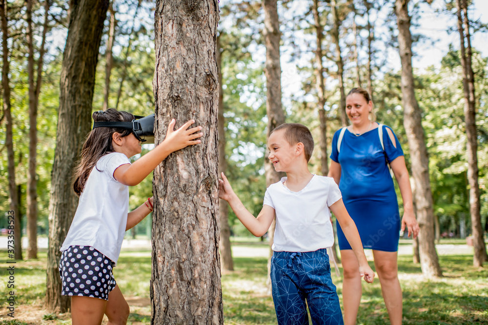 Fototapeta premium School children in white t shirts having fun with virtual reality headset outdoor in the park