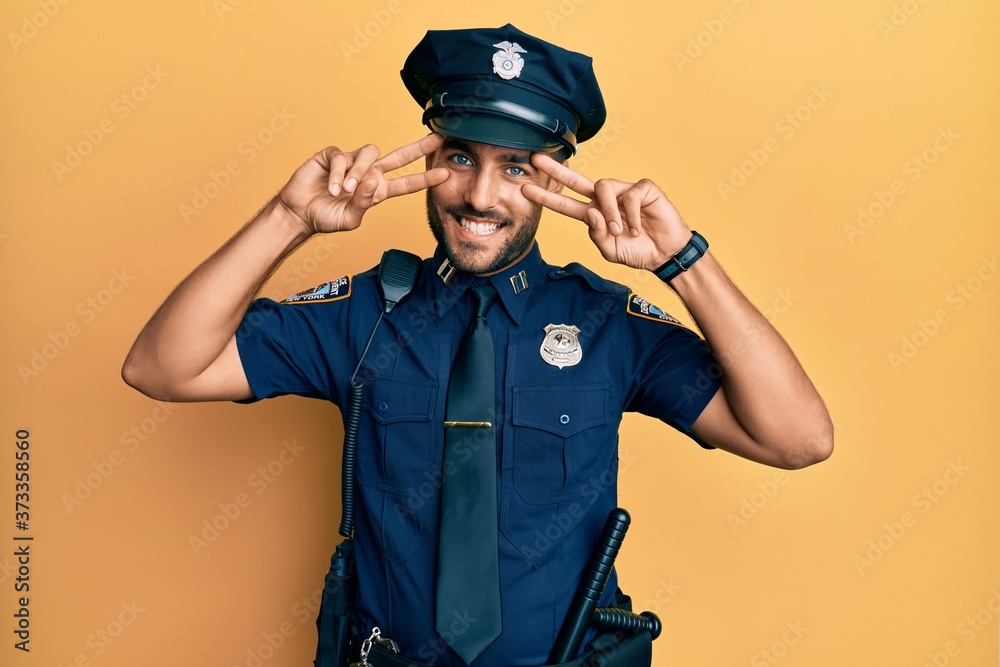 Handsome hispanic man wearing police uniform doing peace symbol with fingers over face, smiling cheerful showing victory Handsome hispanic man wearing police uniform doing peace symbol with fingers over face, smiling cheerful showing victory