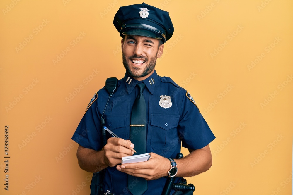 Handsome hispanic man wearing police uniform writing traffic fine winking  looking at the camera with sexy expression, cheerful and happy face. foto  de Stock | Adobe Stock