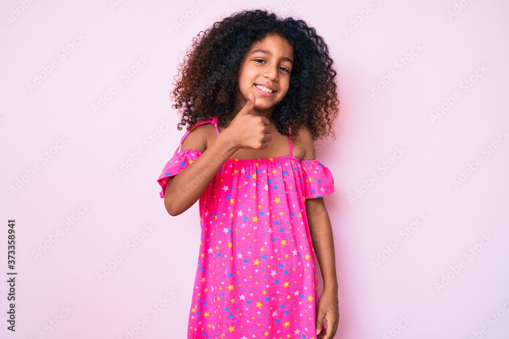 African american child with curly hair wearing casual dress doing happy thumbs up gesture with hand. approving expression looking at the camera showing success. African american child with curly hair wearing casual dress doing happy thumbs up gesture with hand. approving expression looking at the camera showing success.