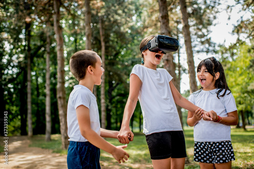 School children in white t shirts having fun with virtual reality headset outdoor in the park