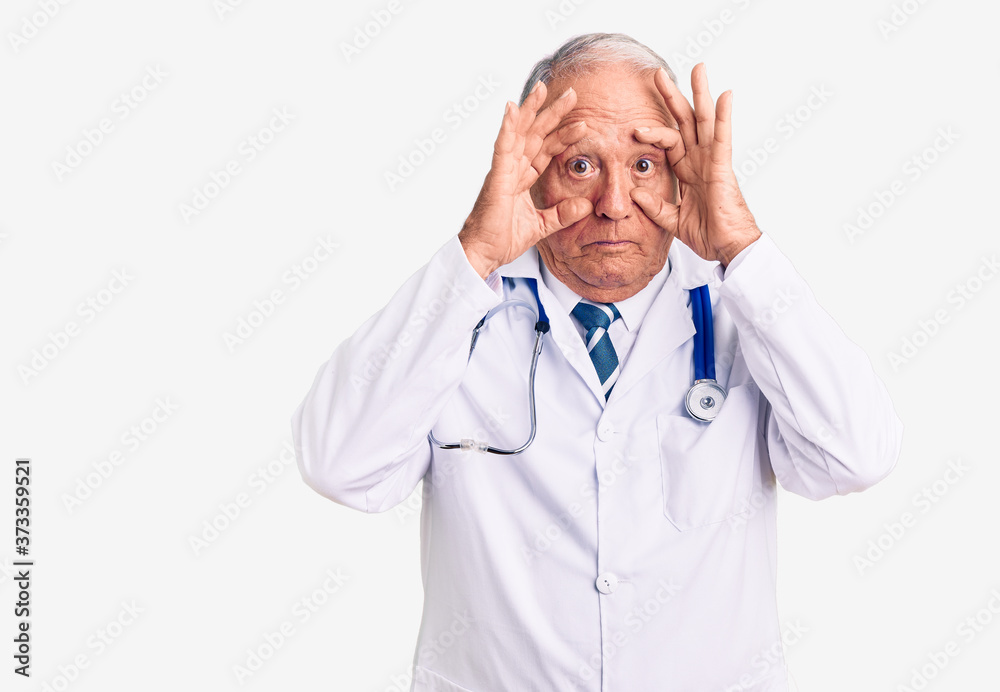 Senior handsome grey-haired man wearing doctor coat and stethoscope trying to open eyes with fingers, sleepy and tired for morning fatigue