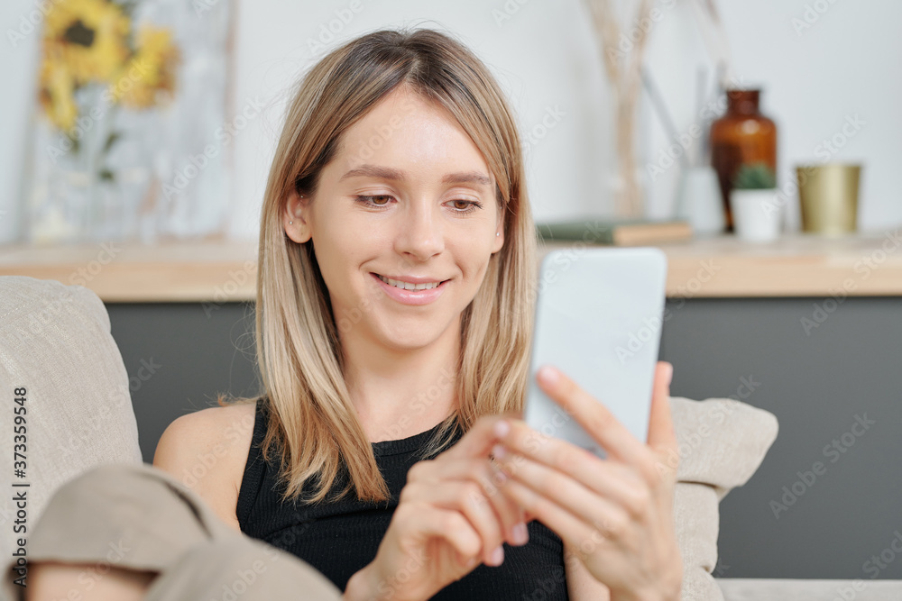 Cheerful millennial with long blond hair looking at photo on smartphone screen Cheerful millennial with long blond hair looking at photo on smartphone screen