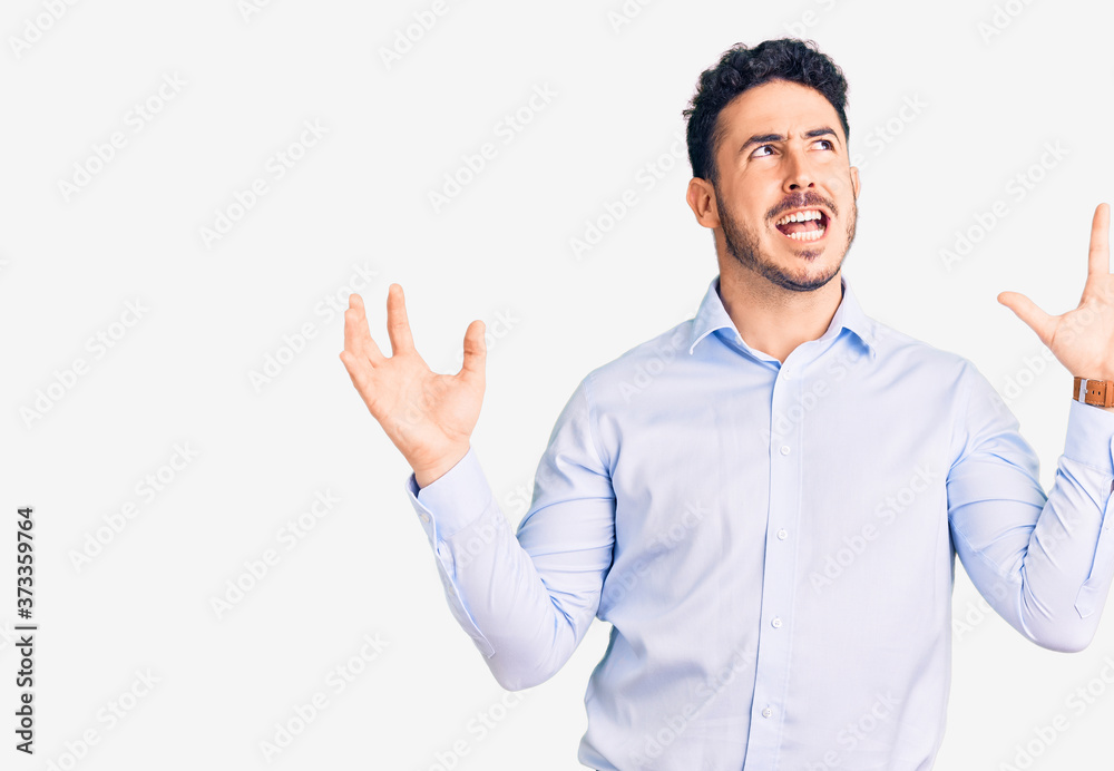 Young hispanic man wearing business clothes crazy and mad shouting and yelling with aggressive expression and arms raised. frustration concept. Young hispanic man wearing business clothes crazy and mad shouting and yelling with aggressive expression and arms raised. frustration concept.