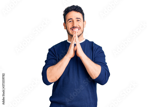 Young hispanic man wearing casual clothes praying with hands together asking for forgiveness smiling confident.