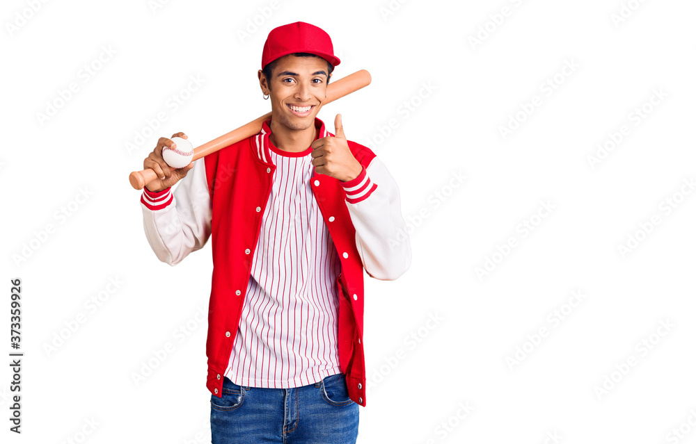 Young african amercian man playing baseball holding bat and ball smiling happy and positive, thumb up doing excellent and approval sign Young african amercian man playing baseball holding bat and ball smiling happy and positive, thumb up doing excellent and approval sign