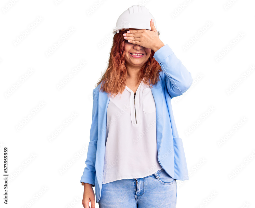 Young latin woman wearing architect hardhat smiling and laughing with hand on face covering eyes for surprise. blind concept. Young latin woman wearing architect hardhat smiling and laughing with hand on face covering eyes for surprise. blind concept.
