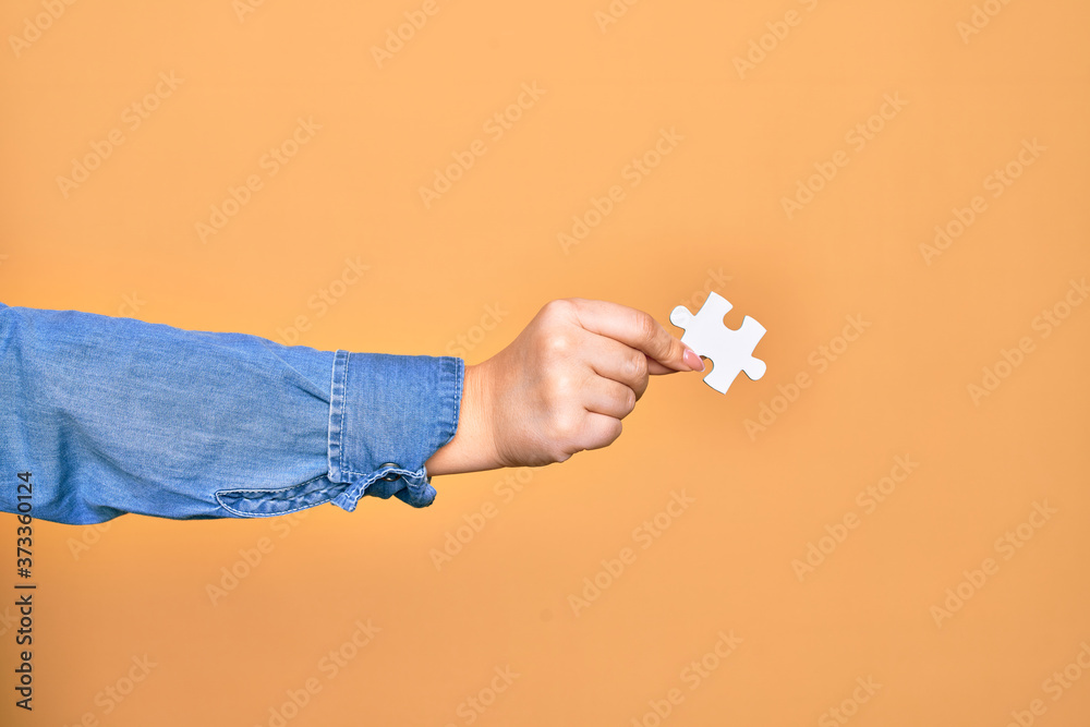 Hand of caucasian young woman holding piece of puzzle over isolated yellow background Hand of caucasian young woman holding piece of puzzle over isolated yellow background