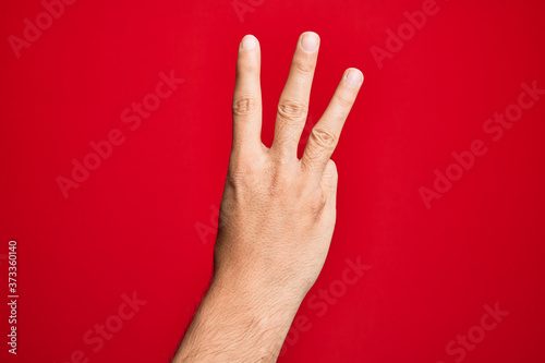 Hand of caucasian young man showing fingers over isolated red background counting number 3 showing three fingers