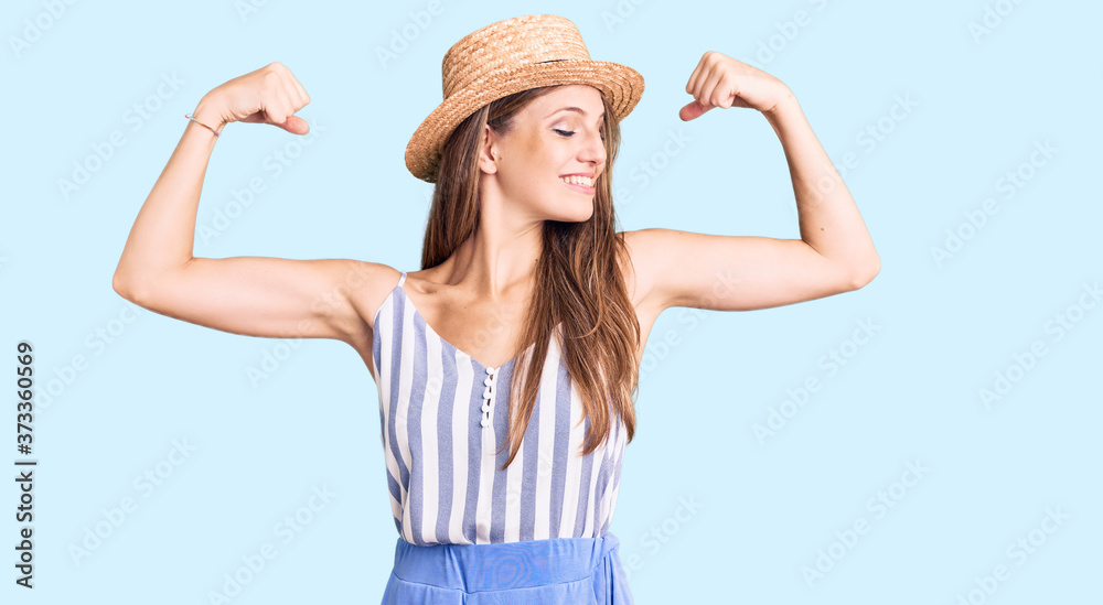Young beautiful blonde woman wearing summer hat showing arms muscles smiling proud. fitness concept. Young beautiful blonde woman wearing summer hat showing arms muscles smiling proud. fitness concept.