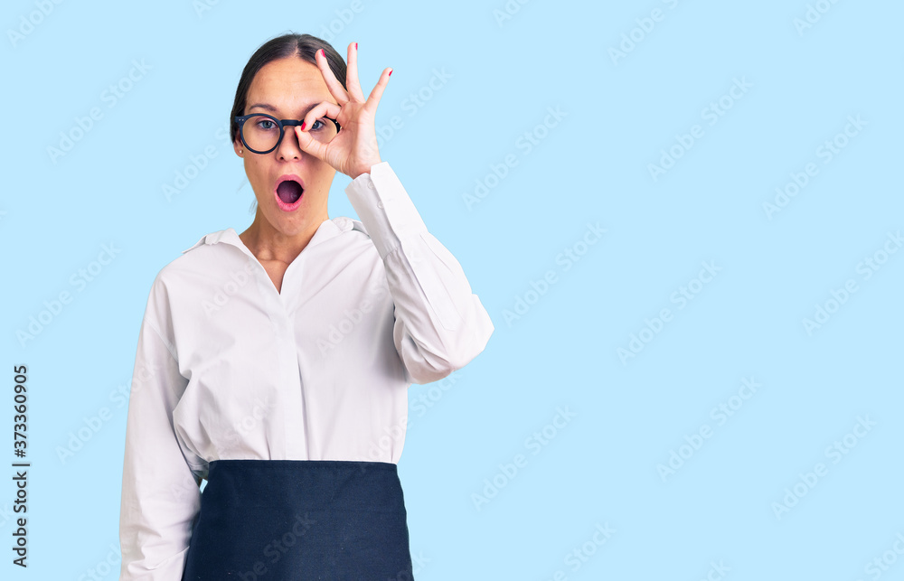 Beautiful brunette young woman wearing professional waitress apron doing ok gesture shocked with surprised face, eye looking through fingers. unbelieving expression. Beautiful brunette young woman wearing professional waitress apron doing ok gesture shocked with surprised face, eye looking through fingers. unbelieving expression.